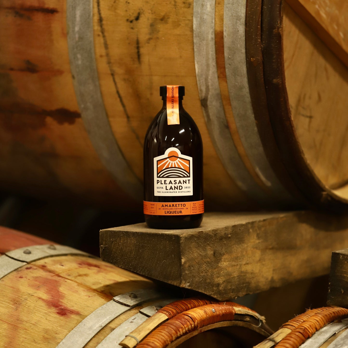 Bottle of Amaretto Liqueur by Pleasant Land Distillery made with Kentish apricots, in front of red wine casks